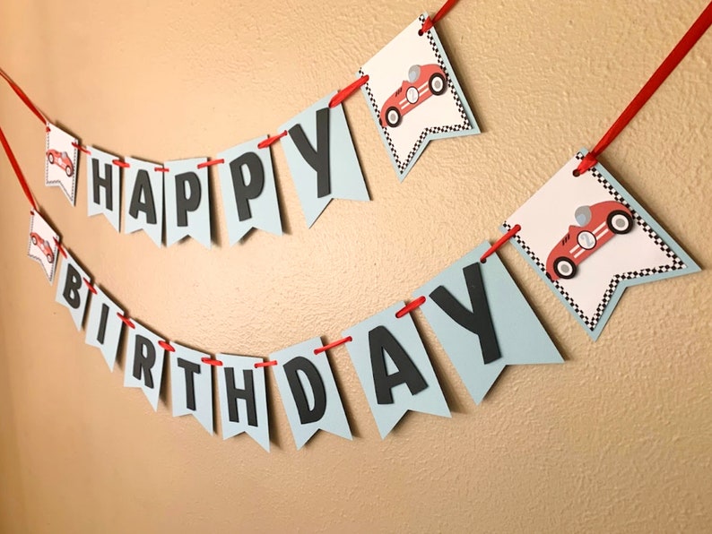 May include: A blue and white banner with the words "Happy Birthday" in black letters. The banner is decorated with red race cars.