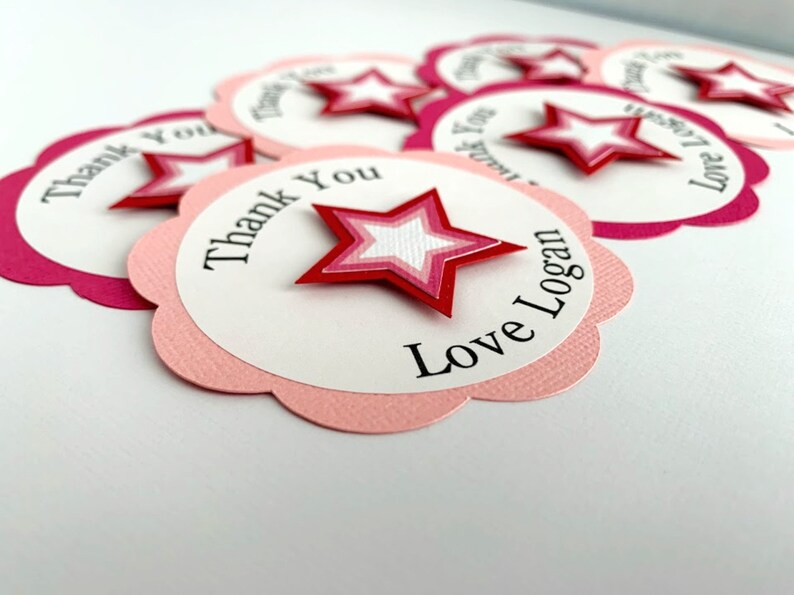 May include: Pink and white scalloped circle thank you tags with a red, pink, and white layered star. The text on the tag reads "Thank You Love Logan".