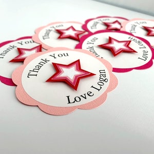 May include: Pink and white scalloped circle thank you tags with a red and white layered star in the center. The text on the tags reads "Thank You" and "Love Logan".