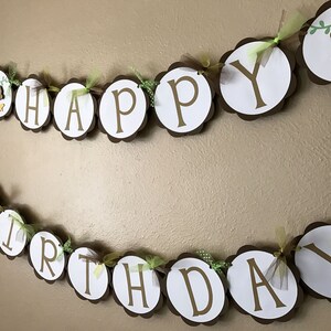 Może przedstawiać: Brązowo-biały baner z napisem "Happy Birthday" złotymi literami. Baner jest ozdobiony zieloną i ż&oacute;łtą wstążką oraz małymi figurkami małp.