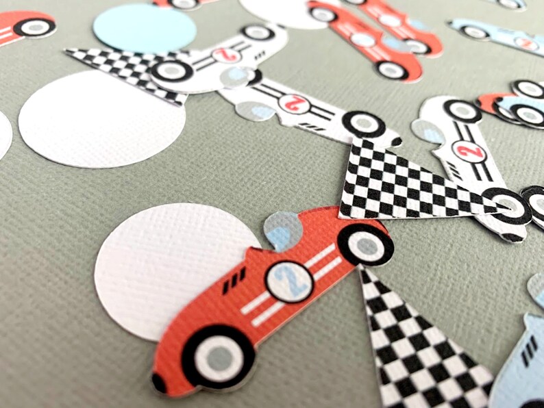 May include: Red, white, and blue race car themed party decorations. The decorations include checkered flags, circles, and cars with the number "2" on them.