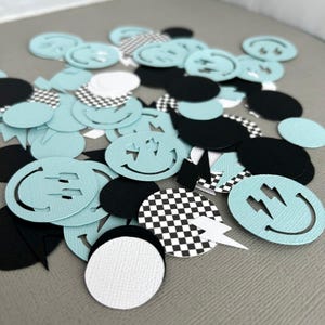 May include: A collection of paper confetti in various shapes and colors. The confetti includes light blue smiley faces, black ovals, white circles, and checkered patterns. Some smiley faces have lightning bolt cutouts.