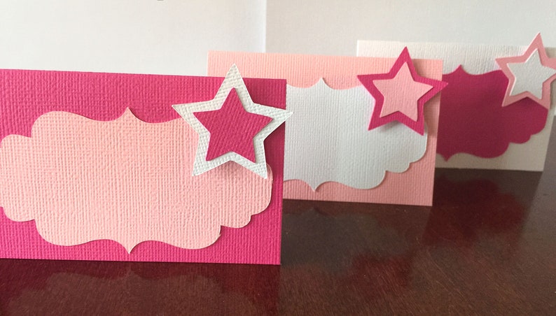 May include: Four pink and white place cards with a scalloped edge and a pink star on each card.
