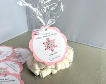Op de afbeelding: Roze en witte cadeautasjes gevuld met witte marshmallows en vastgebonden met een wit lint. De tasjes hebben een roze en wit sneeuwvlokkenontwerp met de tekst "Bedankt voor je komst! Liefs van Emmie".