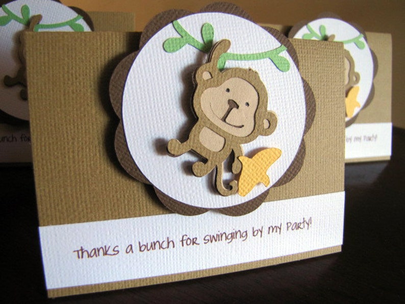May include: A brown thank you card with a white scalloped circle featuring a cartoon monkey hanging from a green vine. The text "thanks a bunch for swinging by my party!" is printed on the card.