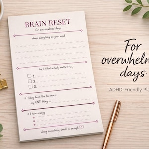 May include: A notepad with the text "BRAIN RESET for overwhelmed days" and prompts to help manage stress. The notepad is on a light wood surface, with a pen, coffee cup, and gold paper clip nearby. The planner is labeled "ADHD-Friendly".