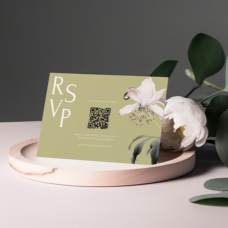 May include: An RSVP card with a floral design, featuring the text "RSVP" in white. The card has a QR code and the text "FIND DETAILS AND TO RSVP OUR WEDDING WEBSITE". The card is light green and is displayed on a wooden tray.