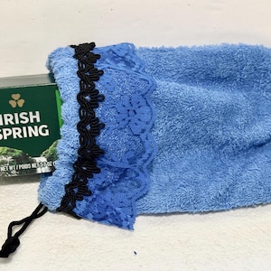 May include: A blue terry cloth drawstring pouch featuring a black decorative trim and a blue lace border. A rectangular green box of Irish Spring soap with the text "IRISH SPRING" and "NET WT / POIDS NET 3.7 OZ" is partially inside the pouch.