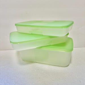 May include: Three rectangular food storage containers stacked on top of each other. The containers are translucent with light green lids. The lids are a solid, bright green color. The containers are empty.