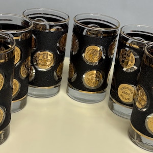 May include: Set of six vintage drinking glasses. Each glass features a black textured band adorned with gold-colored coin-like embellishments. The rims and bases of the glasses are also trimmed in gold, creating a cohesive and elegant design.