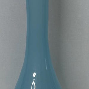 May include: A tall, light blue glass vase with a rounded base and a slender neck. The vase has a flared opening and a circular base. The smooth, glossy surface reflects light, creating highlights. Home decor.