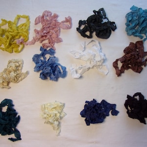 May include: A collection of colorful fabric ribbons in various shades, including yellow, pink, black, and blue. The ribbons are arranged in small, ruffled bundles, suitable for crafting or decorative purposes.