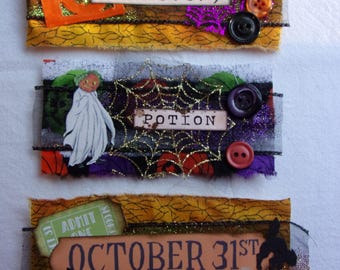 May include: Three rectangular fabric patches featuring Halloween themes. The top patch says "Cemetery" with an orange pumpkin cutout and buttons. The middle patch says "Potion" with a ghost and spiderweb. The bottom patch says "October 31st" with a bone.