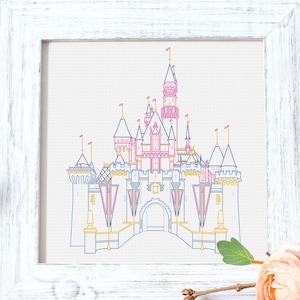 Könnte beinhalten: Ein weißer Rahmen mit einer bunten Linienzeichnung von Aschenputtels Schloss. Das Schloss ist rosa, blau und gelb. Der Rahmen steht auf einer Holzoberfläche mit einer Sukkulentenpflanze und einer rosa Blume.