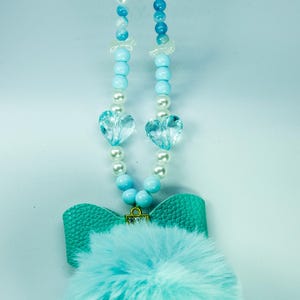 May include: A light blue faux fur pom-pom keychain with a turquoise leather bow and a beaded chain with white and blue beads and crystal heart charms.
