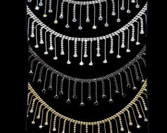 May include: Four strands of fringe trim featuring metallic settings and clear or colored rhinestones. Each strand consists of a horizontal chain with vertical dangling segments of varying lengths, each ending in a single round rhinestone.