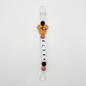 May include: A pacifier clip featuring a clear plastic attachment at the top, followed by a brown spherical bead and a tan waffle-shaped charm. Below are white cube beads spelling the name ELIZA, separated by dark brown and dusty rose beads.