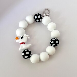 May include: A white and black beaded bracelet featuring a Zero charm from The Nightmare Before Christmas. The bracelet has white beads, black beads with white polka dots, and a silver clasp.