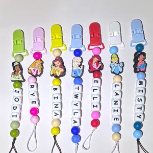 Puede incluir: Una colección de clips para chupetes de bebé con personajes de princesas de dibujos animados. Cada clip tiene un clip, una cuenta y un dije de princesa de diferente color, con un nombre escrito con cuentas de letras blancas. Los nombres incluyen: Jodi, Rye, Bina, Twyla, Elli, Lanie y Misty.