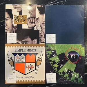 Peut inclure: Quatre albums vinyles du groupe Simple Minds. Une pochette présente un collage de visages, une autre est bleu marine uni, une troisième a un motif de bouclier et la dernière un motif géométrique vert et noir.