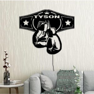 Puede incluir: Arte de pared de metal negro con un dise&ntilde;o de guante de boxeo con un cintur&oacute;n de campeonato. El cintur&oacute;n tiene la palabra "TYSON" y una corona encima de la palabra.