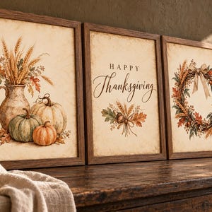 May include: A set of three framed wall art prints with dark wood frames. The left print shows a pitcher with wheat and pumpkins. The center print features the text Happy Thanksgiving with autumn leaves. The right print displays a wreath with a bow.