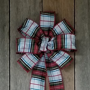 May include: A large plaid bow with red, white, black, and green stripes. The bow is made of ribbon and has long, flowing tails. The bow is likely for decoration, possibly for a holiday or gift.