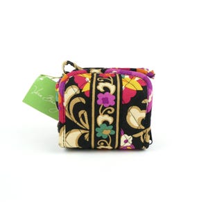 May include: A small, square Vera Bradley cosmetic bag with a colorful floral pattern in black, pink, yellow, and purple. The bag has a zipper closure and a small handle. A green tag with the Vera Bradley logo is attached.