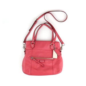 May include: A coral-colored leather tote bag with a shoulder strap and top handles. The bag features a front zipper pocket, silver-tone hardware, and a hang tag. The Coach logo is visible on the front.