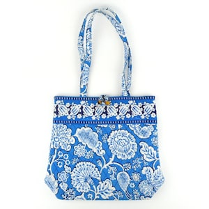 May include: A quilted tote bag featuring a vibrant blue and white floral pattern. The bag has two matching fabric shoulder straps, a rectangular body with a diamond-stitched texture, and a horizontal band across the top with a floral border.