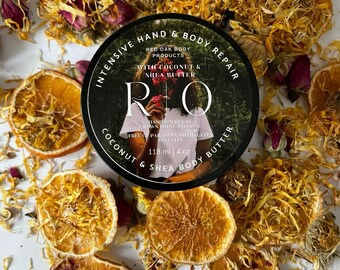 Può includere: Un barattolo nero di Intensive Hand & Body Repair di Red Oak Body Products con cocco e burro di karité. Il barattolo è circondato da fette d'arancia essiccate, petali di fiori gialli e boccioli di rosa rosa. Il barattolo contiene 118 ml di burro per il corpo.