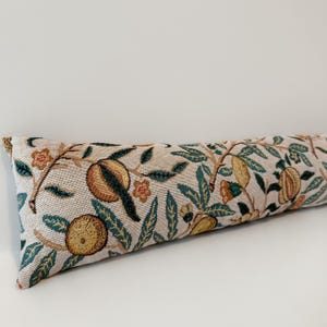 Peut inclure: Un butoir de porte rectangulaire et long, avec un fond beige et un motif r&eacute;p&eacute;t&eacute; de fruits, de feuilles et de fleurs dans des tons de vert, jaune et marron. Le butoir de porte est en tissu tiss&eacute;.