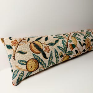 May include: A long, rectangular decorative pillow with a beige background and a detailed floral pattern. The pattern includes brown, yellow, and green fruit and leaves. The pillow is likely made of a woven fabric.