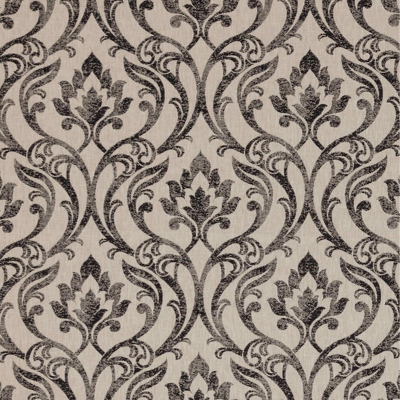 May include: Close-up of a fabric with a repeating damask pattern. The design features dark grey floral motifs and scrolling vines against a light beige background. The pattern is symmetrical and detailed.