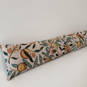Peut inclure: Un butoir de porte long et cylindrique avec un fond beige et un motif r&eacute;p&eacute;t&eacute; d'oranges, de feuilles et de fleurs dans des tons de jaune, vert et orange. Le butoir de porte mesure environ 61 cm de long.