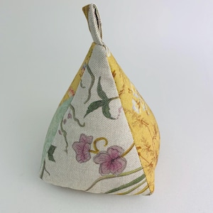 Könnte beinhalten: Ein dreieckiger Türstopper mit einem floralen Muster in Gelb-, Grün- und Rosatönen. Der Türstopper hat oben einen Schlaufe.