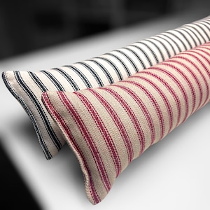 Puede incluir: Dos cojines de tope de puerta a rayas. Uno es blanco con rayas negras y el otro es blanco con rayas rojas.