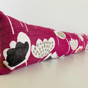 May include: A pink and white patterned doorstop with a floral design. The doorstop is made of fabric and has a rectangular shape.