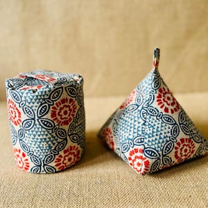 Op de afbeelding: Twee stoffen kussens in een blauw en rood bloemenpatroon. Een kussen is cilindrisch en de andere heeft de vorm van een piramide.