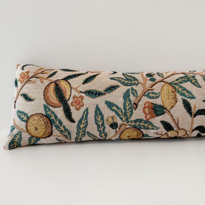 Peut inclure: Long, coussin rectangulaire avec un motif r&eacute;p&eacute;t&eacute; de fruits, de feuilles et de fleurs dans des tons de marron, vert et orange sur un fond beige. Coussin de style traversin.