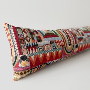 以下が含まれることがあります： 鮮やかな幾何学模様の長方形の装飾用枕。枕は、赤、オレンジ、青、緑の形をしたタペストリーのようなデザインが特徴です。デザインには、三角形、正方形、円が含まれています。枕の長さは約75cmです。