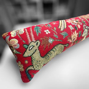 May include: Red doorstop with a colourful tapestry design featuring a stylised deer, flowers, and other abstract patterns.