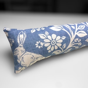 Puede incluir: Un tapón de puerta azul y blanco con un patrón floral y un diseño de conejo. El tapón de puerta está hecho de tela y tiene una forma rectangular.