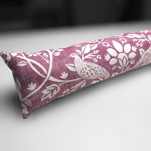 Può includere: Un fermaporta lungo, rosa e bianco con un motivo floreale e di uccelli. Il fermaporta è fatto di tessuto e ha una forma cilindrica.