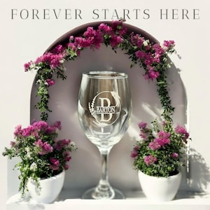Puede incluir: Una copa de vino transparente con un monograma personalizado y el nombre "Barton" grabado. La copa está rodeada de flores rosas y el texto "FOREVER STARTS HERE".