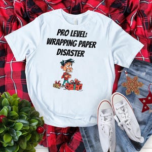 Divertente maglietta natalizia con il testo "Pro-Level Wrapping Paper Disaster" con un personaggio dei cartoni animati esausto. Regalo perfetto per le risate di Natale