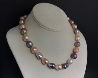 May include: A necklace of irregularly shaped pearls in shades of pink, purple, and cream. The pearls are strung together, creating a statement piece. The necklace is displayed on a white bust against a dark background.