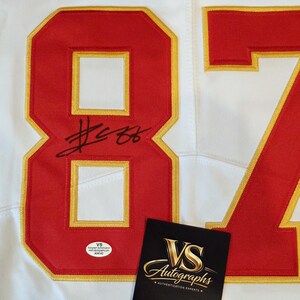 May include: White jersey with red and gold accents, featuring the number 87. The jersey has an autograph and a VS Autographs authentication sticker and card.