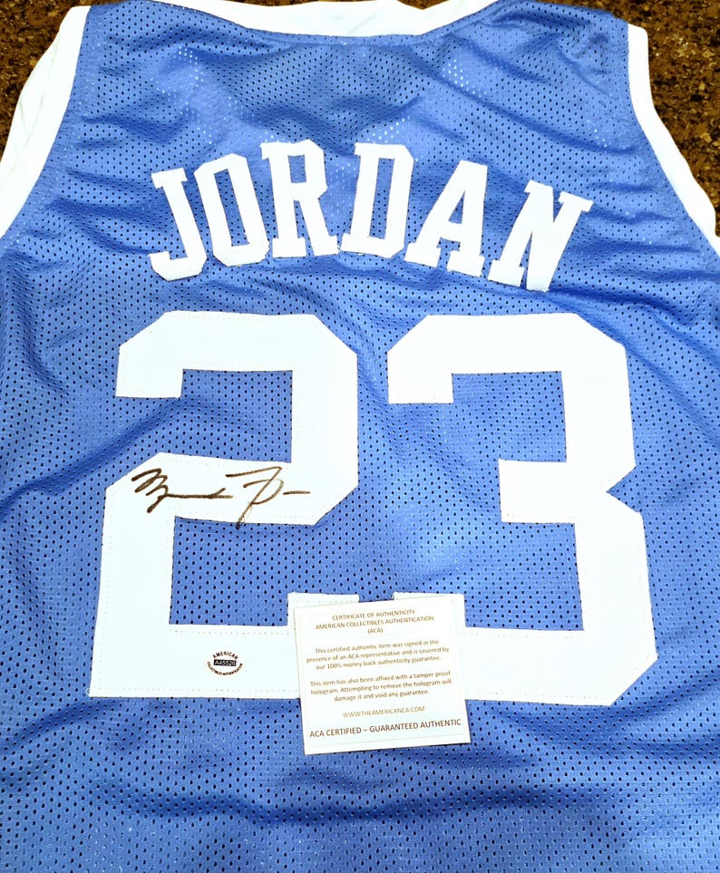 May include: Light blue mesh jersey with the name "JORDAN" and the number "23" in white. The jersey has a white collar and armbands. Includes a signature and an authentication certificate.