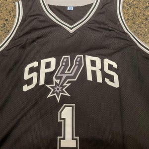 May include: Black XL basketball jersey with the word "SPURS" in white block letters. The jersey features the Spurs logo and the number "1" in white. The jersey has a V-neck and white and gray trim.